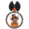 Cute Highland cow wearing a jack-o-lantern beanie while sitting inside a pumpkin.