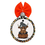 Cute Highland cow wearing a black skull beanie while sitting on a leopard-print pumpkin.