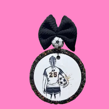 Decorative car ornament with a soccer player design and black bow on a blurred green background