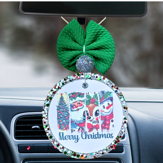 Car ornament with Christmas design and green bow on a car dashboard.