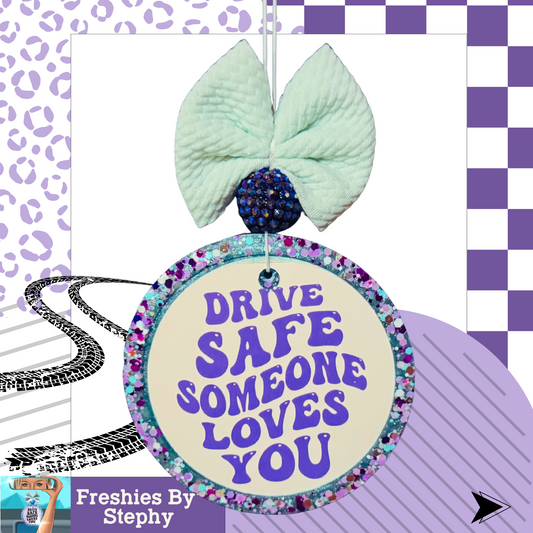Car air freshener with a bow and 'Drive Safe Someone Loves You' message on a checkered background